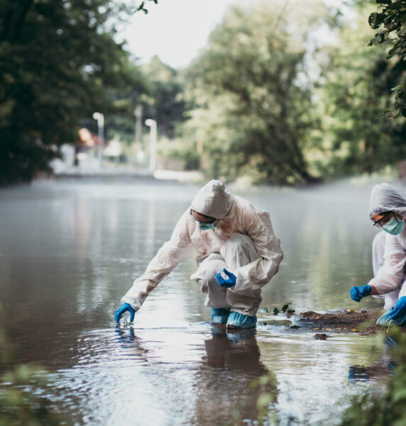 Two scientists in protective suits taking water samples from the river.