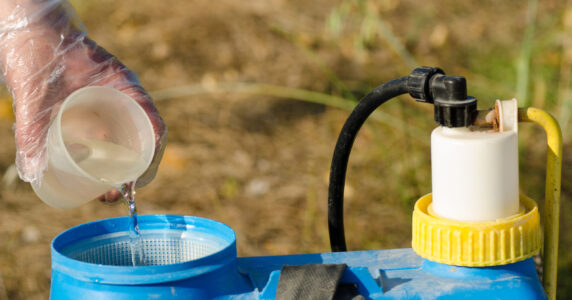 Pesticide being added into  a sprayer using a measuring cup